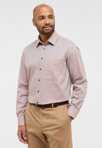 Camicia button-up rosa chiaro con un discreto motivo a spina di pesce, taschino sul petto, bottoni marroni e maniche lunghe, abbinata a pantaloni beige.