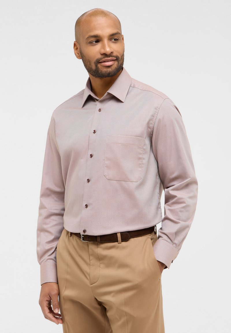 Camicia button-up rosa chiaro con un discreto motivo a spina di pesce, taschino sul petto, bottoni marroni e maniche lunghe, abbinata a pantaloni beige.