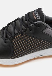 Fekete Skechers golfcipő fekete fűzővel, csíkozott oldalsó panelekkel, párnázott nyakkal és fehér talppal, amelyen az "ARCH FIT" felirat olvasható.