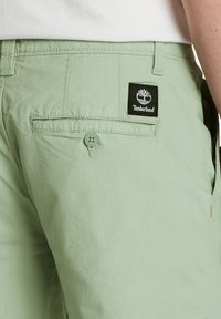 Jasnozielone bawełniane szorty z tylną kieszenią z czarną naszywką logo Timberland, z zapięciem na guzik oraz widocznymi detalami ściegów.