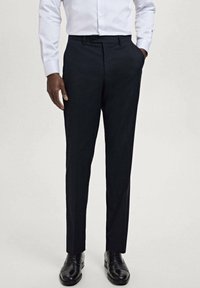 Tailored navy trousers made of woven fabric, featuring a flat front, side pockets, and a slim-fit design. Styled with black shoes.