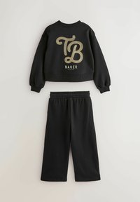 Sort to-delt outfit bestående af en cropped sweatshirt med lange ærmer, der har guld "TB" og "Baker" tekst, parret med matchende brede bukser.