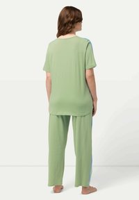 Grön bomullsloungewear-set bestående av en kortärmad topp och lösa byxor med blå sidodetaljer. Mjuk textur, avslappnad passform.