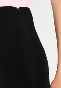 Jupe noire à texture lisse, dotée d'une fermeture éclair latérale et d'une coupe ajustée, présentée avec un haut rose.