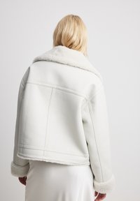 Giacca in pelle bianca con ampio colletto e polsini in shearling morbido. Design corto con dettagli di cucitura visibili e una finitura liscia.