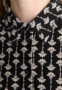 Black shirt with a white floral pattern, featuring a pointed collar, button closure, and a textured fabric.