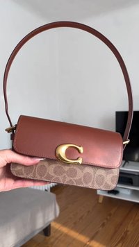 Καφέ δερμάτινη τσάντα ώμου με χρυσή αγκράφα σε σχήμα "C", με μοτίβο στο κάτω μέρος και δομημένο ορθογώνιο σχήμα.