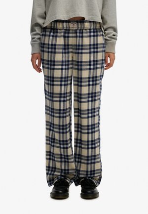 Osoba w szerokich spodniach w beżowo-granatową kratę z elastyczną talią i czarnych butach, ubrana w szary top z długim rękawem.