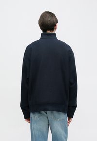 Πουλόβερ σε σκούρο μπλε ναυτικό χρώμα με ψηλό γιακά, κατασκευασμένο από απαλό ύφασμα με μείγμα βαμβακιού· διαθέτει άνετη εφαρμογή και ριμπ μανσέτες και τελείωμα.
