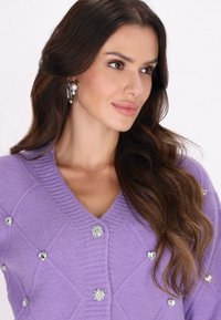 Lila Strickjacke mit V-Ausschnitt, die mit Diamantmustern versehen und mit kristallähnlichen Akzenten verziert ist.