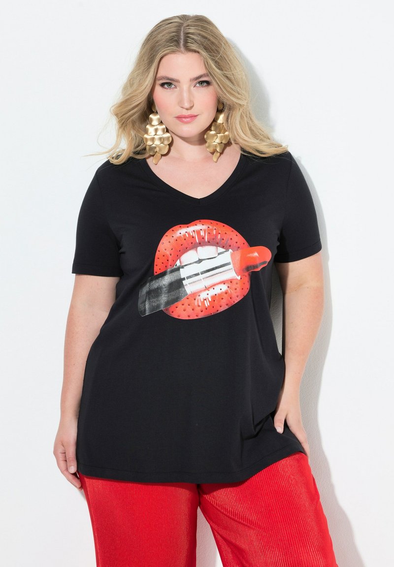 Czarny T-shirt z krótkim rękawem i dekoltem w serek z dużym nadrukiem czerwonych ust i szminki, zestawiony z czerwonymi spodenkami prążkowanymi. Złote efektowne kolczyki.