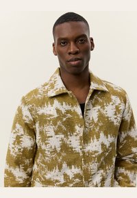 Green and white patterned button-up shirt with a spread collar and textured fabric, featuring two buttons on the front and a relaxed fit.