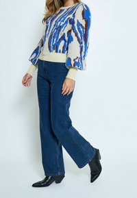 Stickad tröja med mönster i blått, brunt och krämfärgat, puffärmar och ribbad nederkant. Inpassad med mörkblå högmidjade jeans och svarta ankelstövlar.