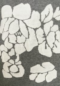 Motifs floraux tricotés blancs sur un fond de tissu gris avec des pétales texturés et des formes de feuilles formant un motif regroupé.