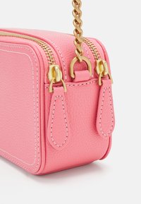 Borsa in pelle rosa con superficie testurizzata, dotata di accessori in metallo dorato per la chiusura lampo e una tracolla con catena intrecciata. Include cuciture dettagliate.