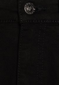 Musta farkkukangas, jossa on vinoraitainen kohokuvio. Varustettu hopeisella napilla, jossa on sana "SPIRIT", ja tummilla kontrastitikkauksilla.