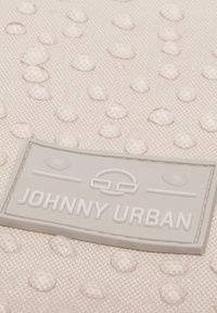 Světle růžová strukturovaná tkanina s vyvýšenými kruhovými tečkami a šedou gumovou etiketou s nápisem "JOHNNY URBAN", která je výrazně umístěna.