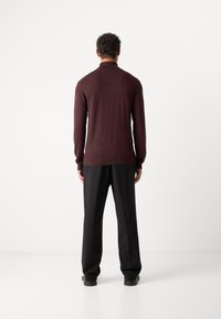 Bordeaux gebreid sweater met een hoge hals, geribbelde zoom en lange mouwen, gecombineerd met zwarte broek. Gladde textuur, aansluitend design.