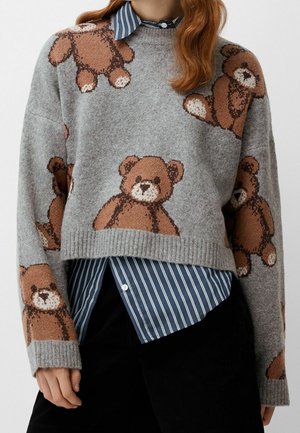 Grijze gebreide trui met bruine teddybeerpatronen, gedragen over een blauw-wit gestreept overhemd met kraag en zwarte broek.