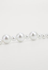 Collier en perles blanches composé de perles rondes brillantes de différentes tailles, avec une texture lisse, présenté sur un fond clair.
