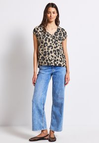 Top in maglia con stampa leopardata in beige e nero, con maniche a cappuccio e scollatura a V. Abbinato a jeans a gamba larga blu chiaro e scarpe slip-on nere.