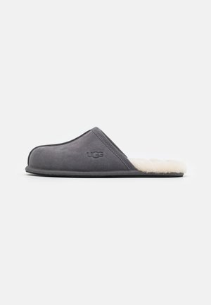Gray suede slip-on slipper with a soft white sheepskin lining and a black rubber sole, featuring a subtle logo on the side.