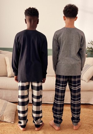 Zwei Kinder in passenden Schlafanzügen: eines trägt ein schwarzes langärmeliges Oberteil und karierte Hose, das andere ein graues Oberteil und ein karierte Hose.