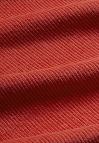 Tessuto di un profondo tono rosso, con una texture a coste e morbidi filamenti vellutati che creano strati ondulati sulla superficie.