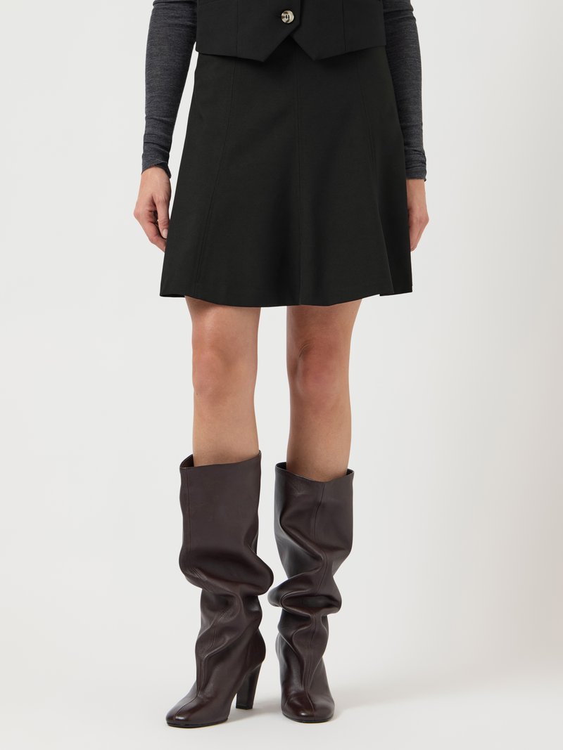 Musta liehuva minihame, jonka kanssa on yllään rentoasenteiset, tummanruskeat polven yläpuolelle ulottuvat nahkasaappaat paksulla korolla. Sileä pinta, ei näkyviä kuvioita.