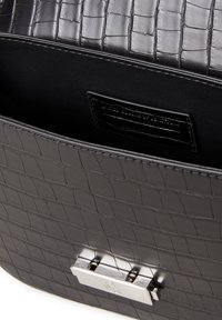 Černá kabelka z kůže s krokodýlím vzorem, vybavená lesklým stříbrným klipem a hladkým interiérem. Štítek uvnitř viditelný. Kompaktní design.