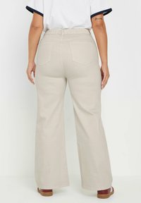 Beige, vida byxor gjorda av bomullstyg med elastisk midjeband och två bakfickor, bärs med bruna sandaler.