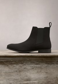 Bottine Chelsea en cuir noir avec panneaux latéraux élastiques et languette, vue de profil sur une surface en bois avec un fond neutre.