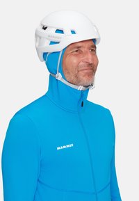 Biała kask wspinaczkowy oraz jasnoniebieska kurtka z zamkiem błyskawicznym, wykonana z teksturowanej tkaniny, z widocznymi szwami i logo na piersi.