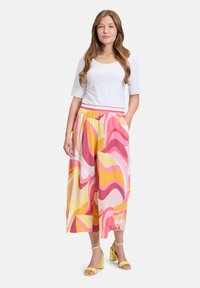 Wielokolorowe spodnie o szerokich nogawkach z falistymi wzorami w różowym, żółtym i białym kolorze, z elastycznym pasem i bocznymi kieszeniami. W połączeniu z białą bluzką.
