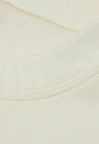 Flødefarvet ribbet strikketøj med en glat tekstur og en blød, strikket halslinning. Subtile, lodrette striber tilføjer visuel interesse.