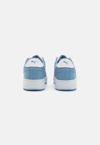 Un par de zapatillas Puma de color azul claro vistas desde atrás, con pestañas en el talón blancas que llevan el logo de Puma y suelas gruesas blancas.