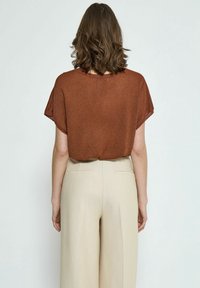 Top marrón de manga corta en una tela ligera y texturizada, combinado con pantalones de pierna ancha beige de talle alto con sutiles pliegues frontales.