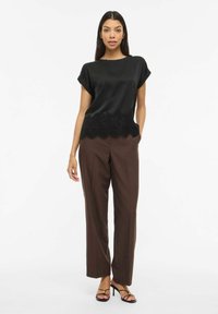 Must siidriidest topp pitsist äärega, kombineeritud pruunide laia säärega pükstega ja mustade rihmikandadega kontsadega. Lihtne siluett ja elegantne disain.