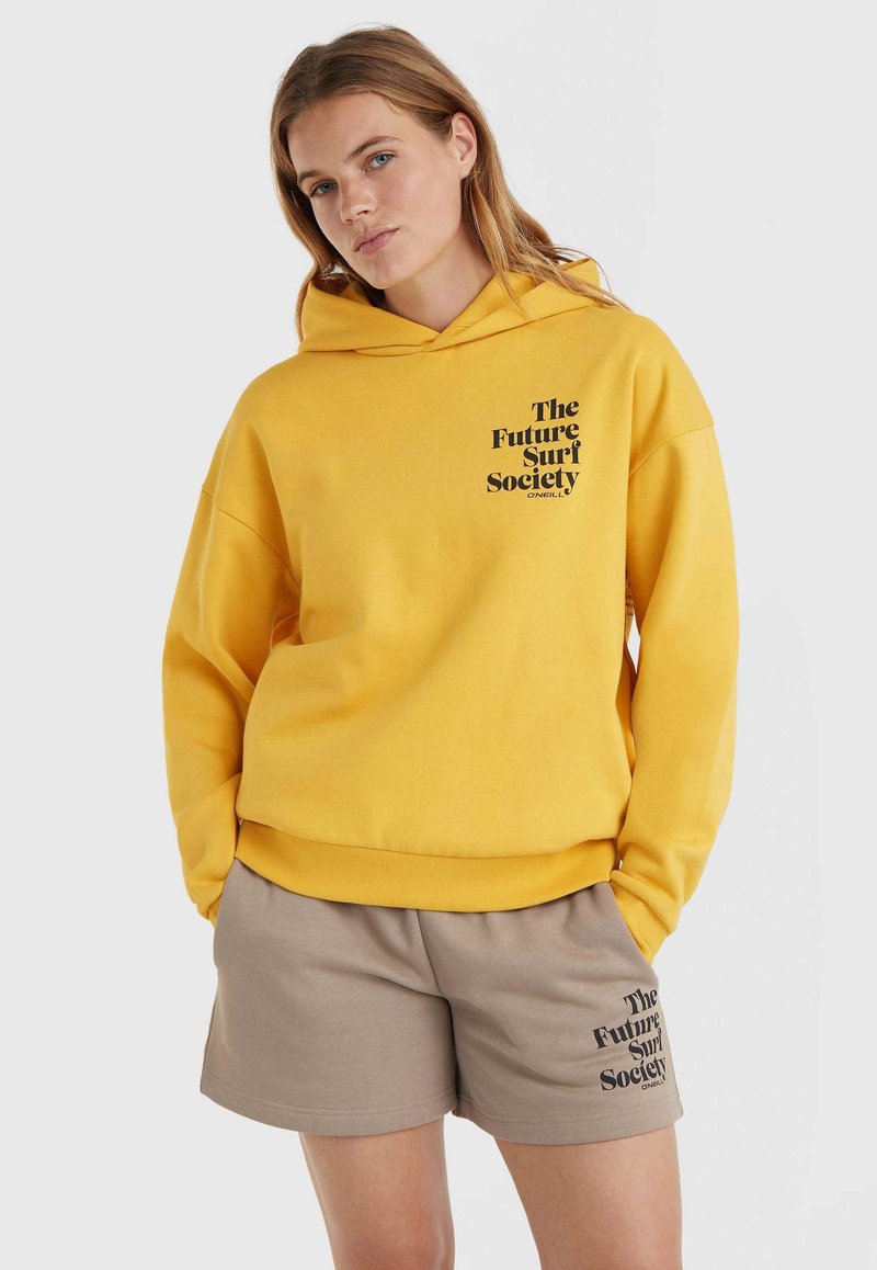Żółta bluza z kapturem z czarnym napisem "The Future Surf Society" z przodu, w połączeniu z beżowymi szortami z tym samym czarnym napisem. Miękki materiał.