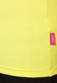 Gul ribbad tygtröja med en sidetikett med rosa accent. Designen inkluderar texturerade vertikala linjer och en figurnära silhuett.