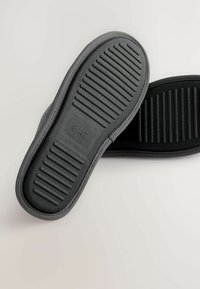 Sive slip-on cipele s teksturiranim gumiranim potplatom, koji imaju izbočine za bolji grip. Dizajn se sastoji od jednostavnog oblika i minimalnih detalja. Veličina 42.