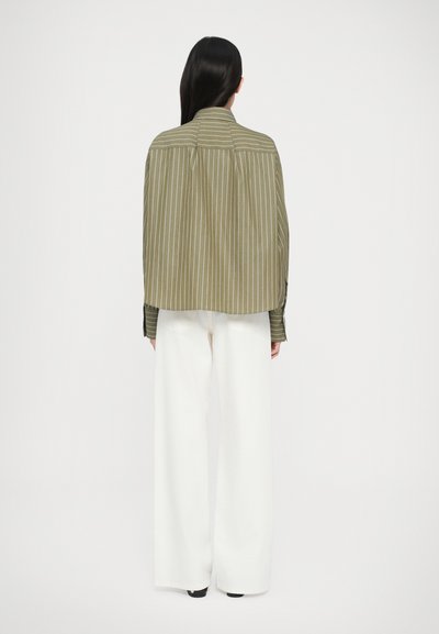 Long-sleeve olive green shirt with white vertical stripes. Features a back pleat and buttoned cuffs, paired with white wide-leg pants.