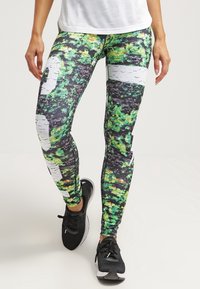 Těsně přiléhající legíny s živým vzorem zelených, žlutých, černých a bílých tvarů, vyrobené z elastického, prodyšného materiálu.