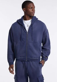 Marinekleurige hoodie met ritssluiting in een zachte stof, voorzien van een voorzak, trekkoordcapuchon en rafelige details, gecombineerd met bijpassende joggingbroeken.