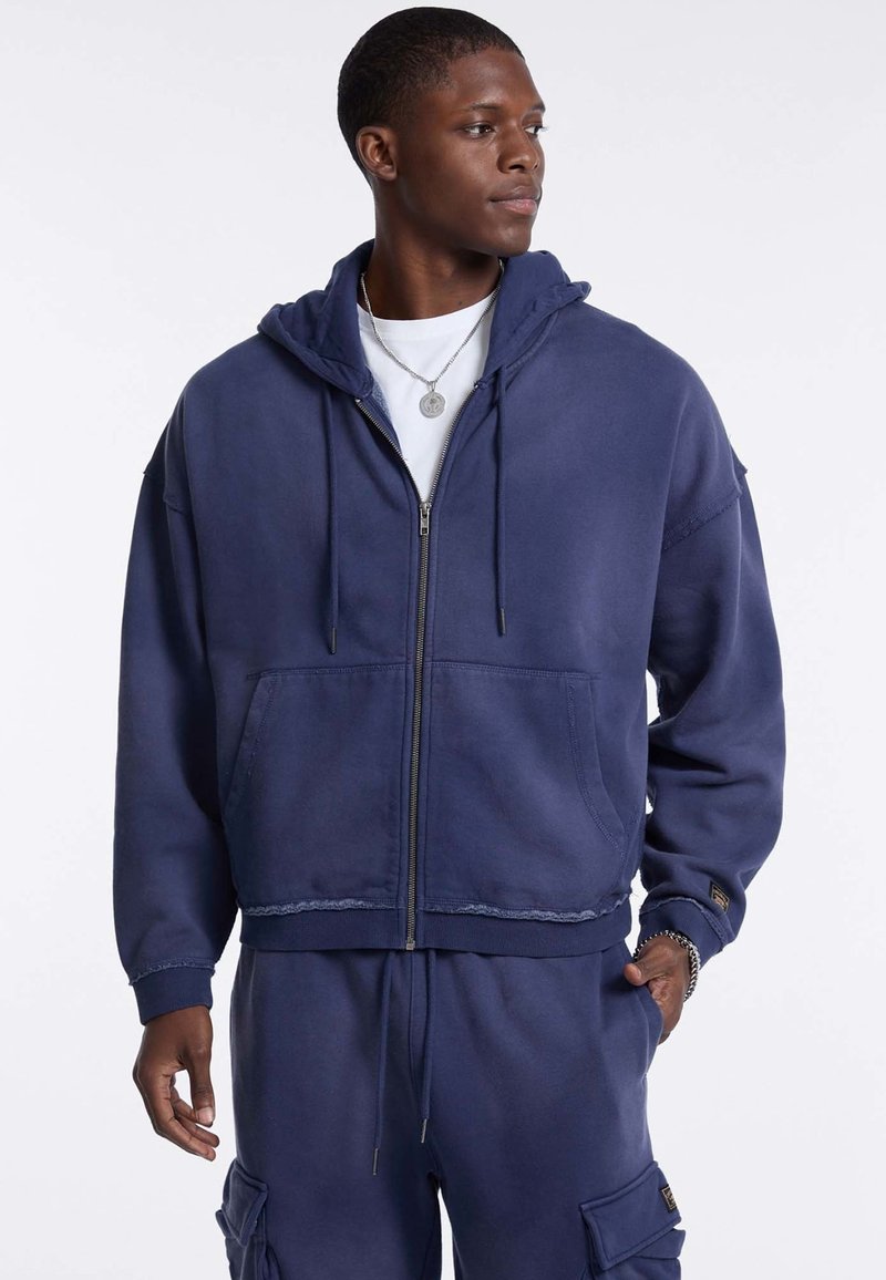 Marinekleurige hoodie met ritssluiting in een zachte stof, voorzien van een voorzak, trekkoordcapuchon en rafelige details, gecombineerd met bijpassende joggingbroeken.