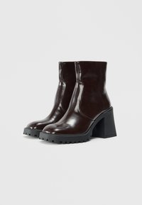 Braune Leder-Stiefeletten mit glänzender Oberfläche, blockierendem Absatz und strukturiertem Gummisohlen. Mit einem eleganten Design und genähten Details.