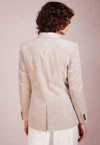Hellbeige Cordblazer mit tailliertem Schnitt, scharfen Revers und geschlitzen Rücken. Verfügt über geknöpfte Manschetten mit drei schwarzen Knöpfen.