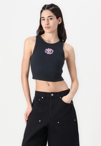 Black ribbed crop top with a round neckline featuring pink embroidered "OBEY" logo. Worn with high-waisted loose black pants.