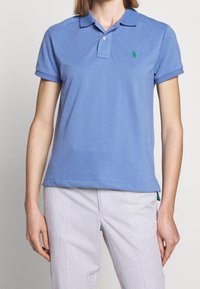 Ljusblå pikétröja i bomull med krage, korta ärmar och en liten grön logga på vänster bröst. Texturerad tyg, klassisk passform.