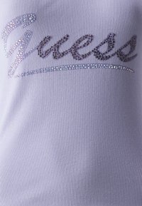Top viola a costine con la scritta "Guess" in strass scintillanti, con una texture liscia e leggermente elastica.